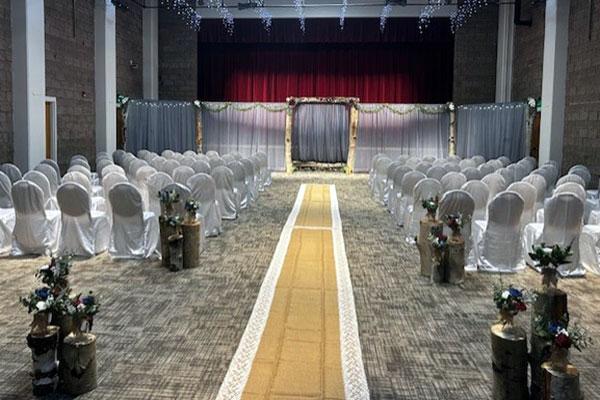 The event hall set up for a wedding with chairs and an aisle.